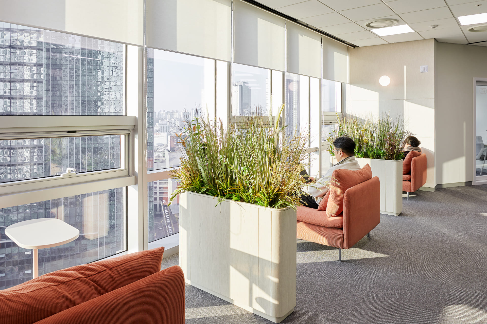 높은 화분 파티션으로 프라이버시를 확보한 창가의 오렌지색 1인용 소파 휴식 공간.jpg