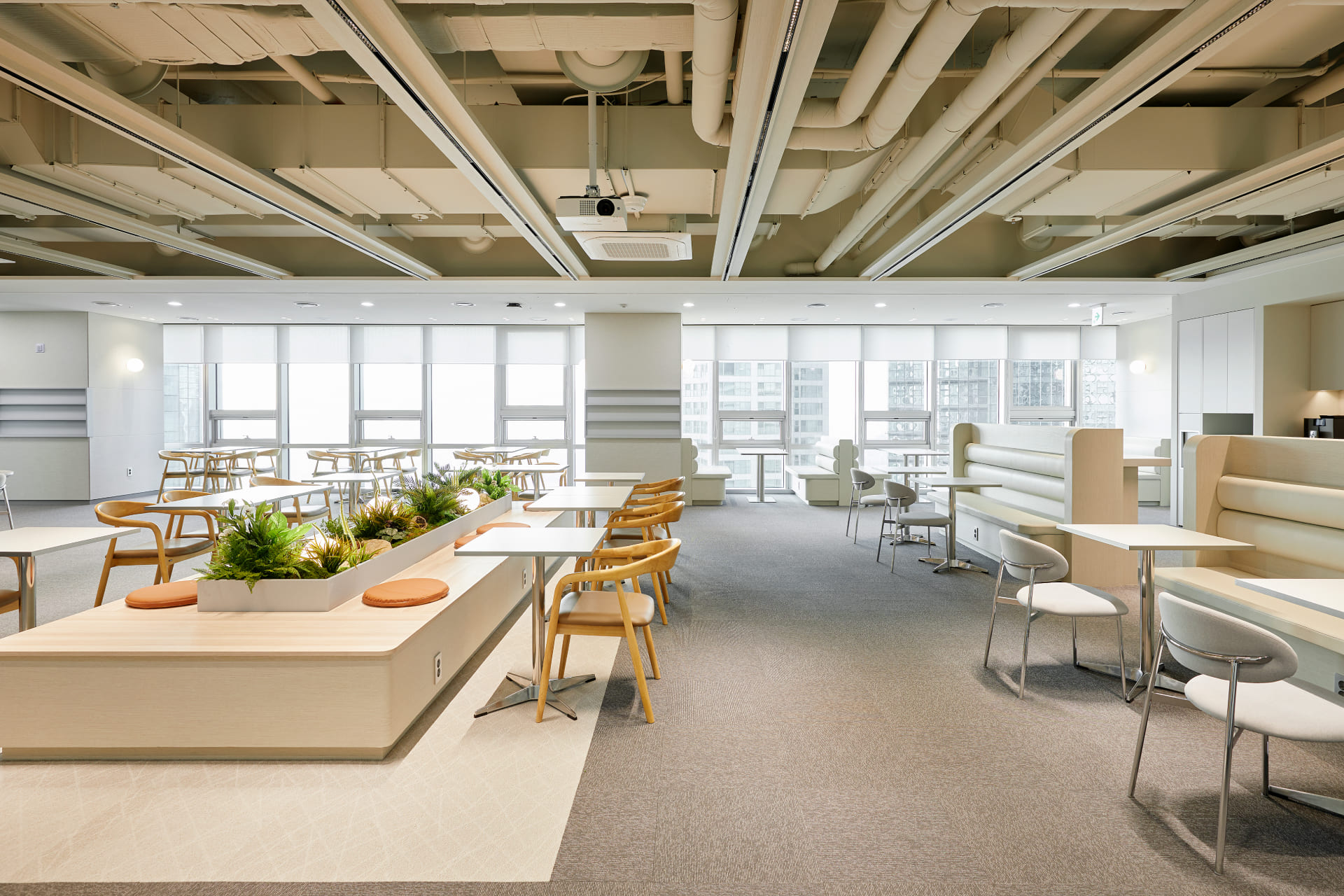 채광이 좋은 통창을 따라 배치된 테이블과 개방감을 주는 노출 천장 디자인의 사무실 라운지.jpg