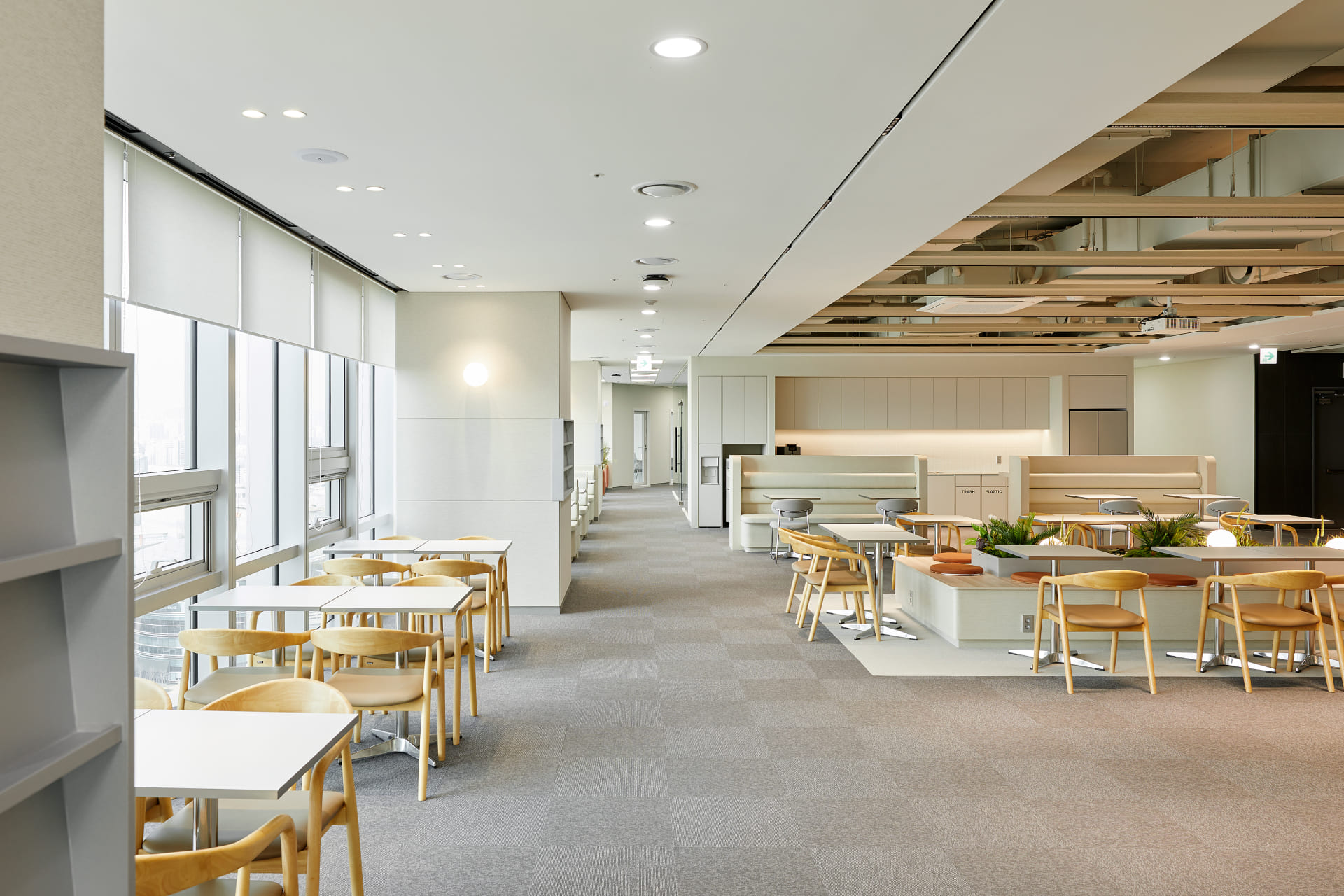 따뜻한 조명과 그레이 카펫이 깔린 복도를 중심으로 좌우 배치된 사무용 가구와 탕비 시설.jpg