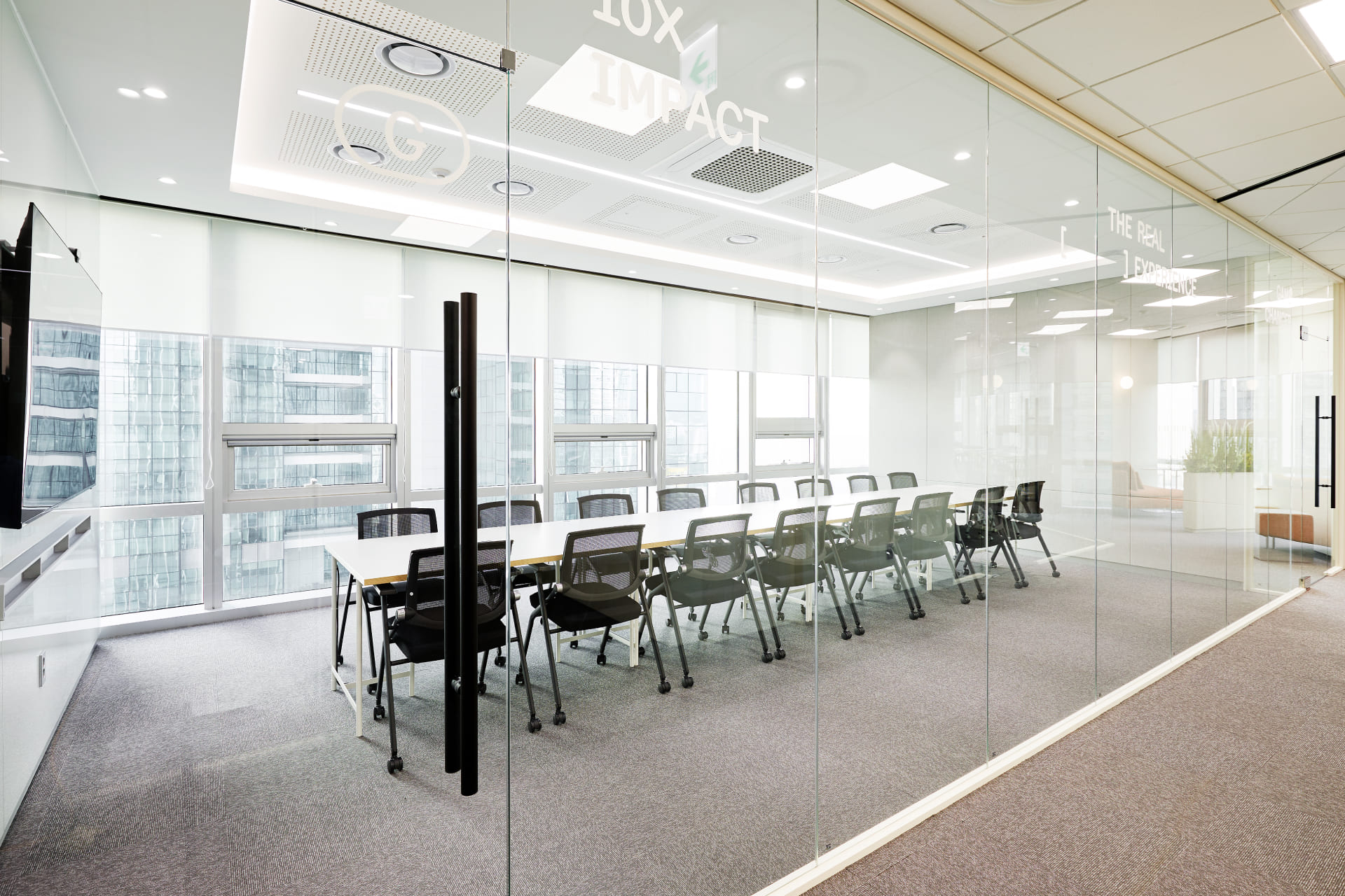 많은 인원을 수용할 수 있는 긴 테이블과 다수의 메쉬 의자가 배치된 통창 구조의 대형 회의실.jpg