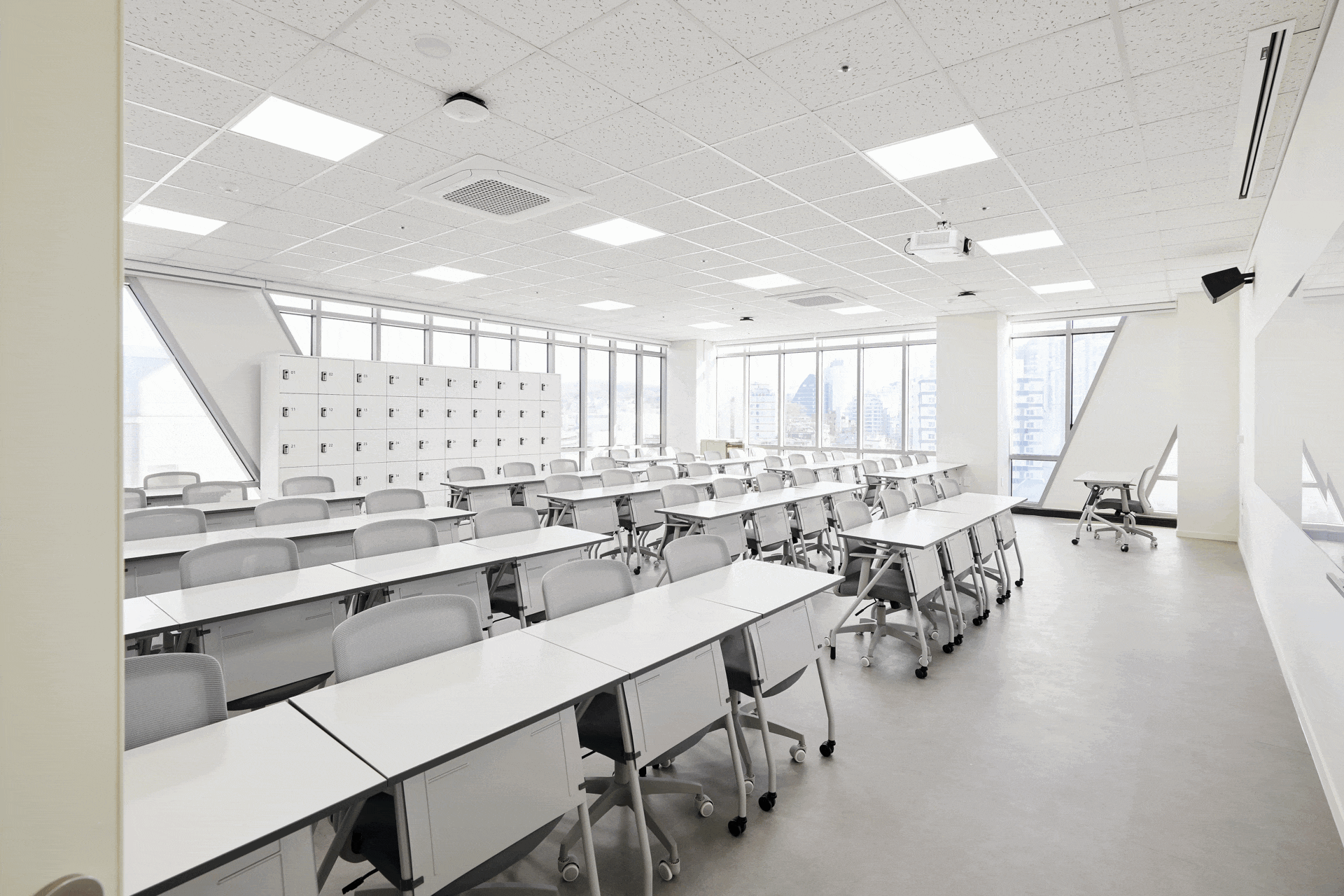 현대적인 인테리어에 화이트 데스크, 메쉬 의자, 천장형 프로젝터와 화이트보드가 완비되어 있는 패스트캠퍼스 강의실 내부 전경.gif