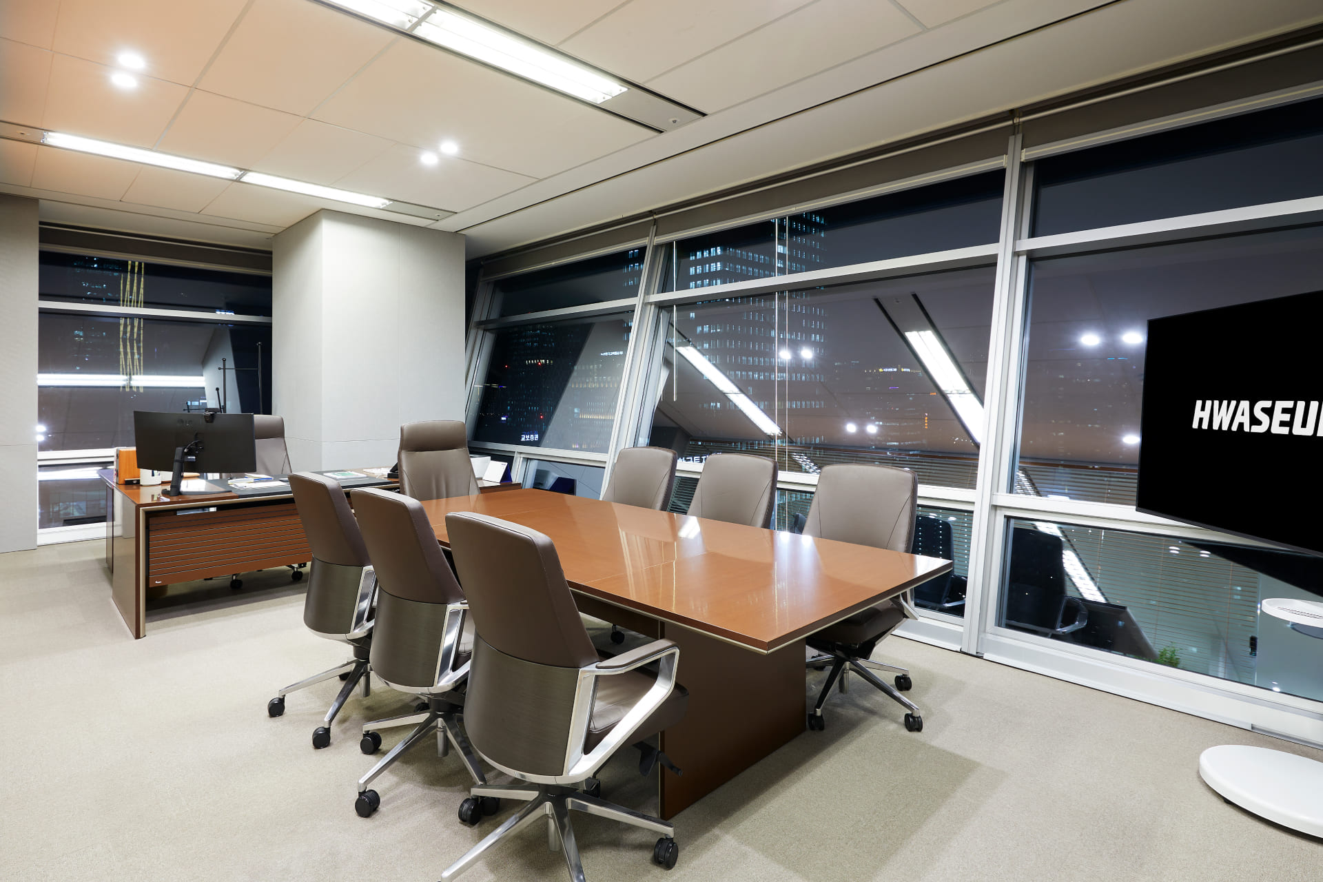 우드 톤 테이블과 가죽 의자, 도심 야경이 보이는 통창이 특징인 고급스러운 분위기의 대표실.jpg