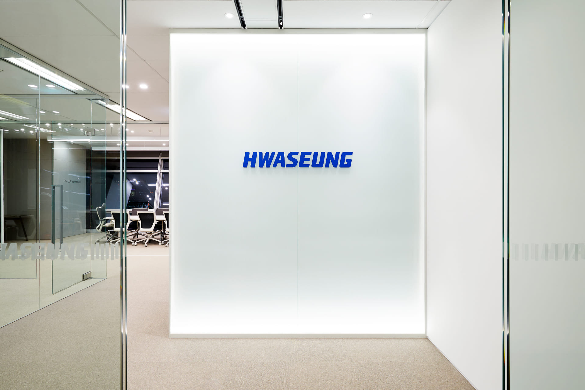 은은한 조명이 매립된 유리 벽 중앙에 부착된 화승(HWASEUNG) 블루 로고 브랜드 월.jpg