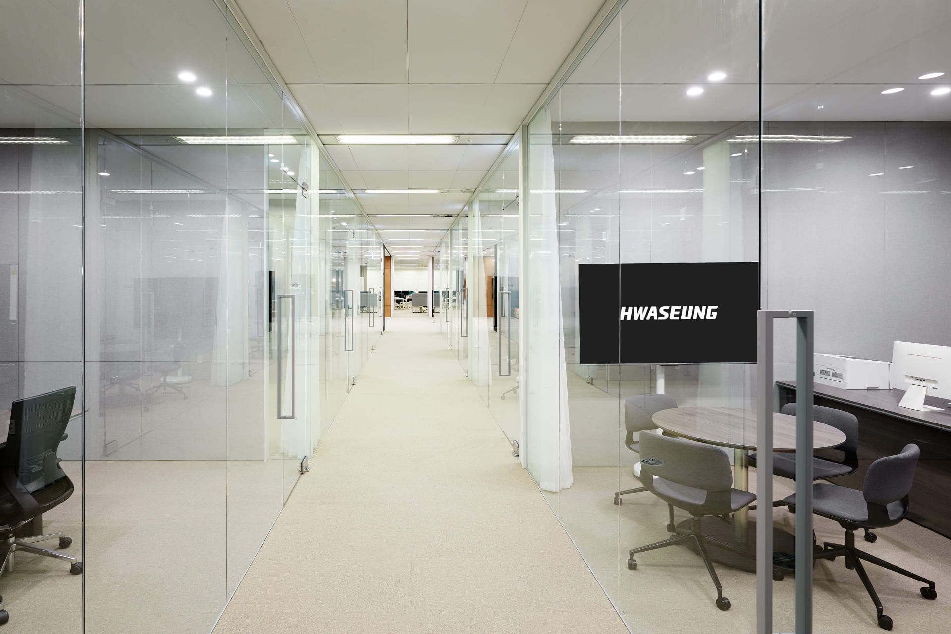 투명한 유리 벽으로 구분된 회의실들이 일렬로 배치된 화이트 톤의 직선형 오피스 복도 인테리어.jpg
