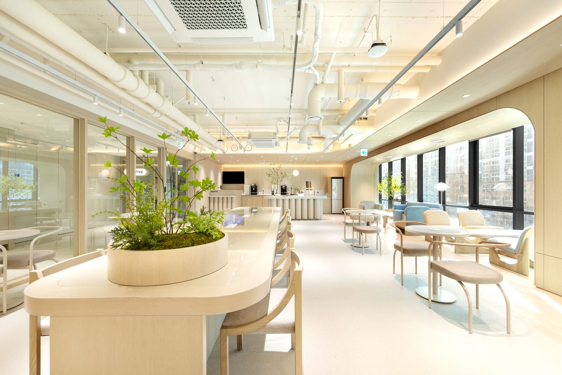패스트파이브 마곡나루점 공용 라운지, 우드톤 곡선 테이블과 식물 플랜터가 어우러진 밝은 카페테리아 공간.jpg