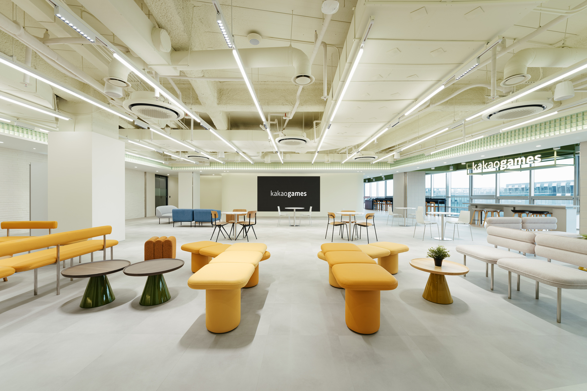 카카오게임즈 사옥 다목적 라운지, 노란색 모듈형 소파와 원목 테이블이 배치된 넓은 오픈 홀 전경.jpg