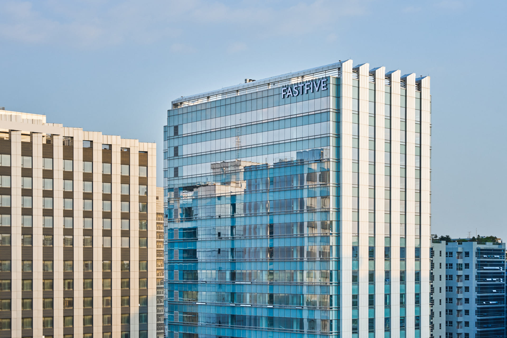 맑은 하늘 아래 패스트파이브(FASTFIVE) 로고가 상단에 부착된 현대적인 통유리 외관의 오피스 빌딩 전경.jpg