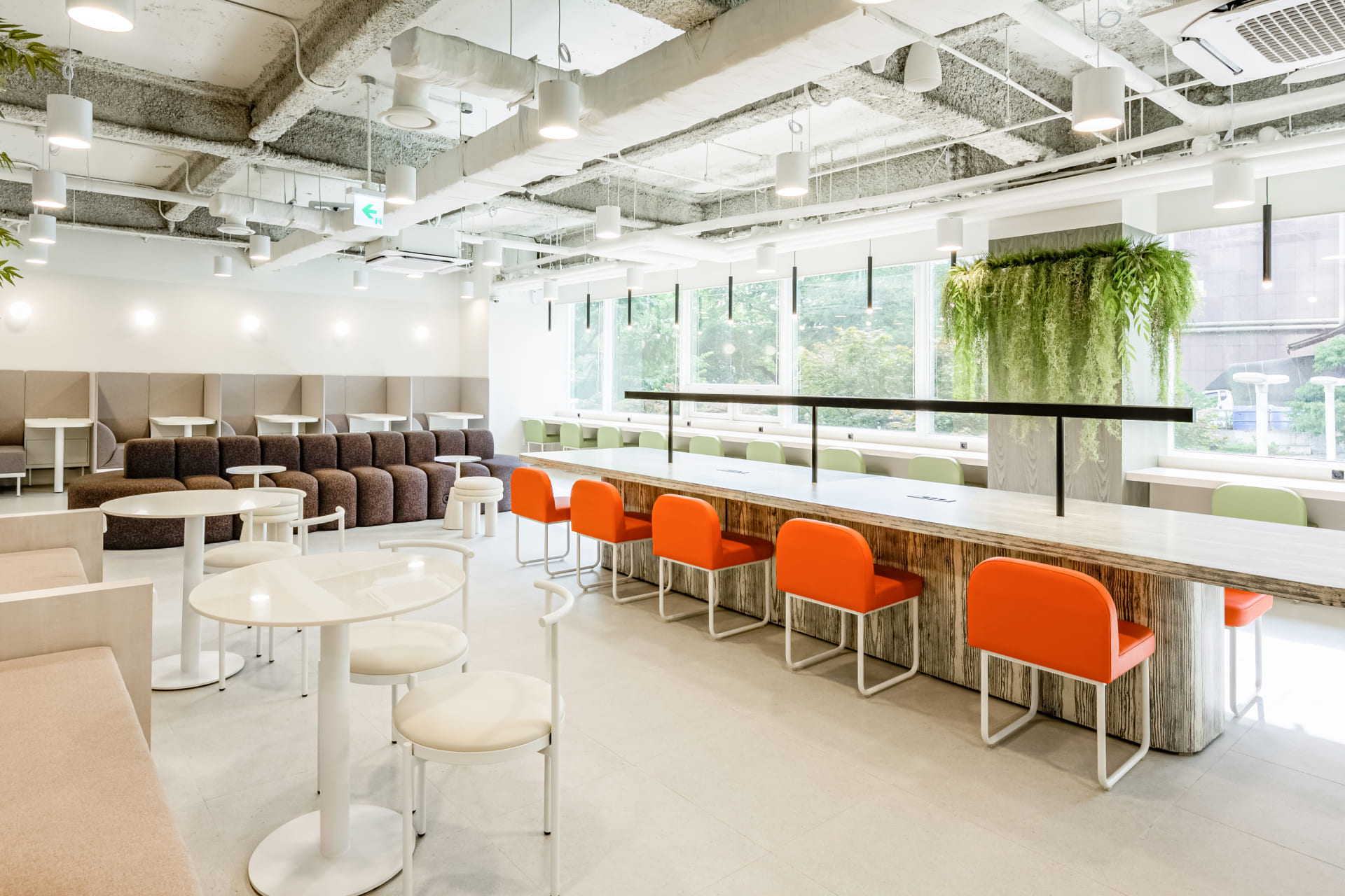 통창을 통해 자연광이 들어오는 밝은 화이트 톤의 공용 업무 공간과 포인트 컬러인 오렌지색 의자.jpg