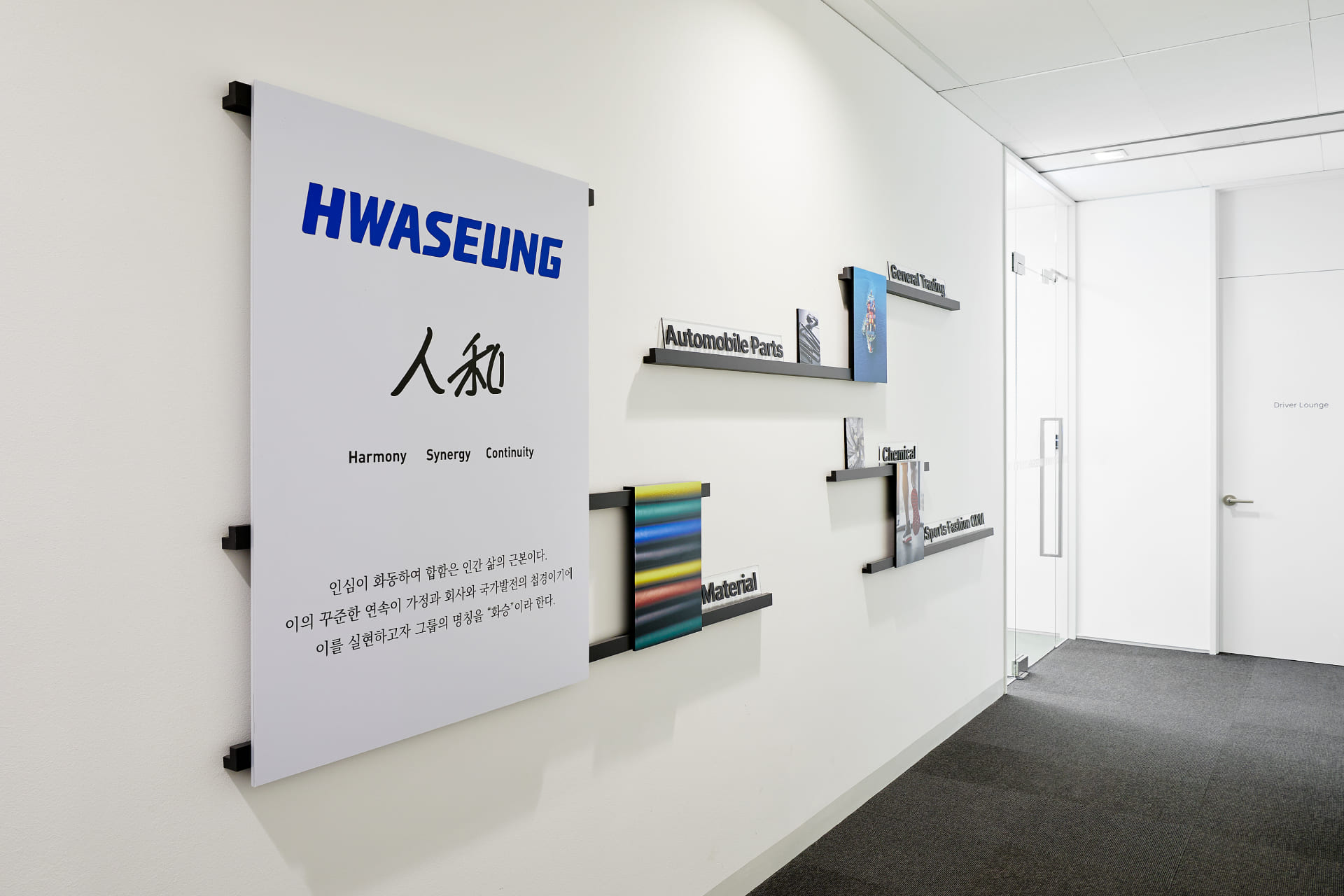 화승 로고와 인화(人和) 정신, 자동차 부품 및 소재 등 주요 사업 영역이 소개된 화이트 톤의 복도 벽면 인테리어.jpg