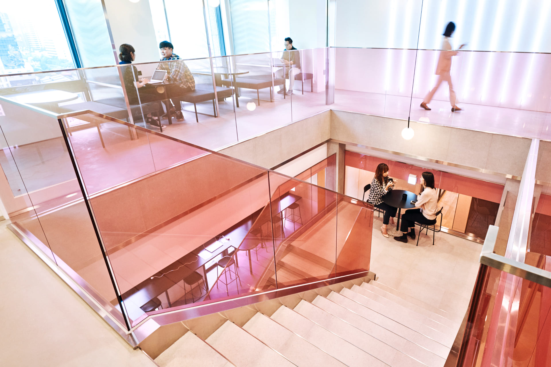 핑크색 유리 난간 계단으로 연결된 복층 구조의 패스트파이브 센터 내부와 층별 미팅 테이블에서 협업 중인 사람들.jpg