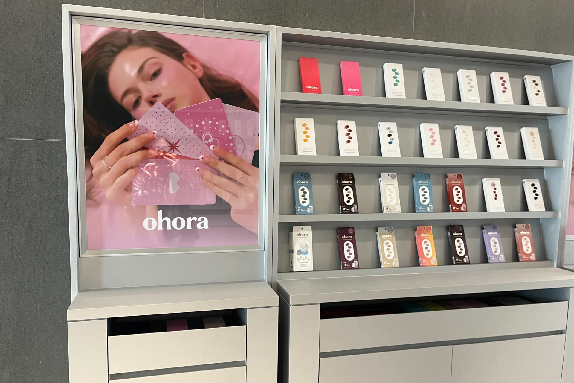 복도에 마련된 오호라(ohora) 제품 쇼룸. 감각적인 브랜드 포스터와 함께 다양한 디자인의 젤네일 패키지가 깔끔하게 진열된 매립형 선반.jpg
