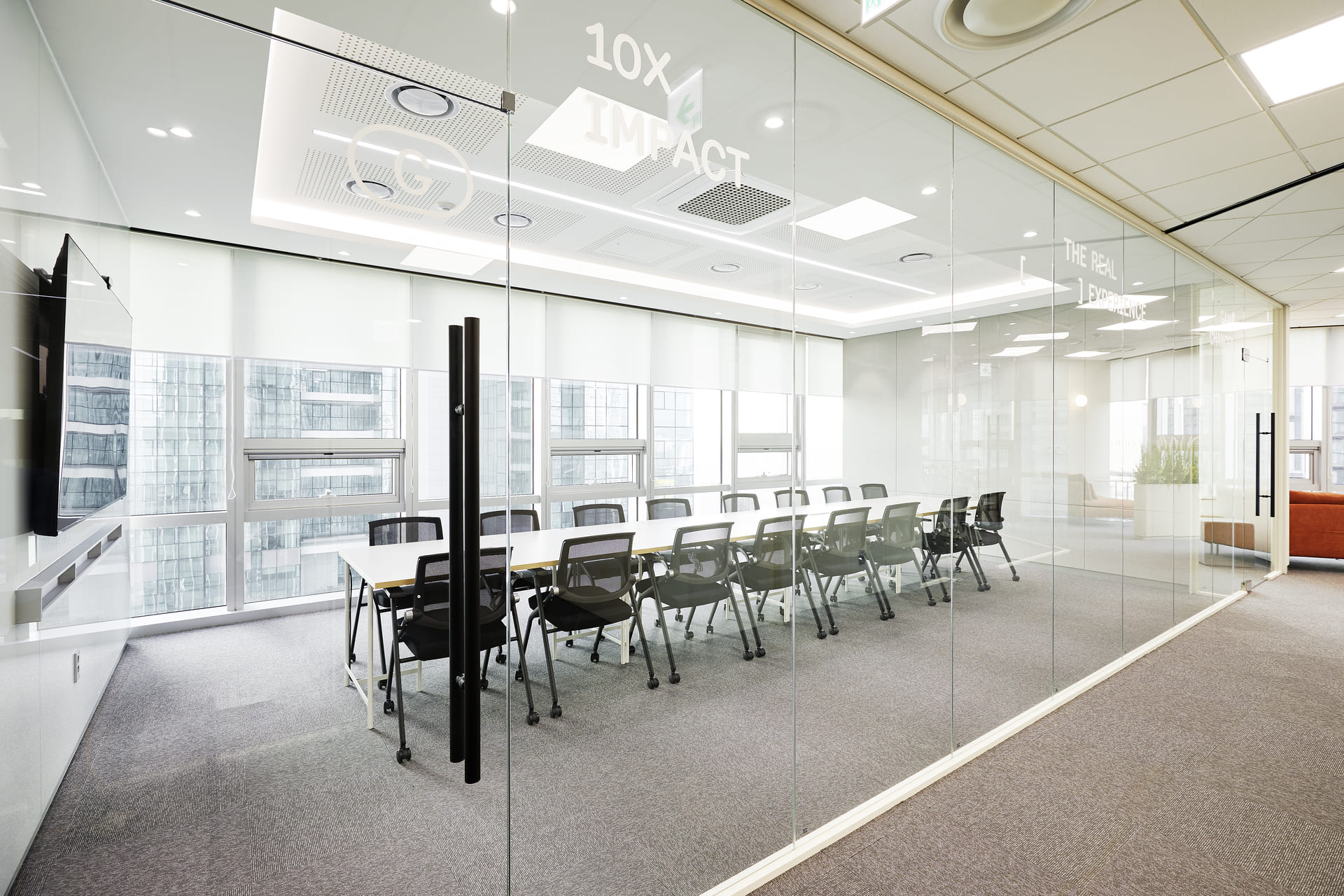 통유리벽에 10X IMPACT 문구가 새겨진 긴 대회의실 테이블과 대형 스크린 모니터가 완비된 사내 회의실 전경.jpg